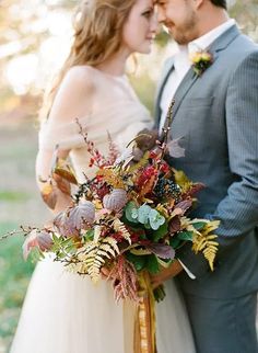 a bride and groom standing next to each other in front of trees with leaves on them