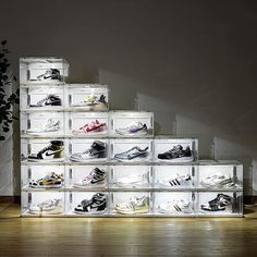 a stack of clear acrylic boxes filled with various pairs of shoes on top of a wooden floor