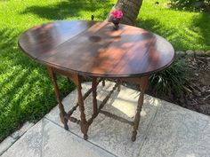 a wooden table sitting on top of a cement floor next to a tree and grass