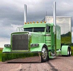 a large green semi truck parked on the side of a road next to a field