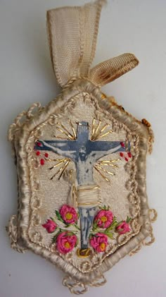 a cross hanging from the side of a wall with flowers on it and a ribbon