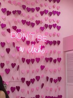 a woman standing in front of a pink wall with hearts on it that says don't be a dicke