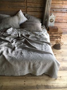 an unmade bed with grey linens in a rustic cabin style bedroom, made from wood planks