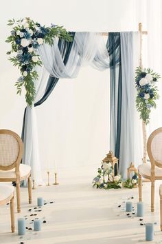 a white and blue wedding arch with flowers, candles and greenery on the floor