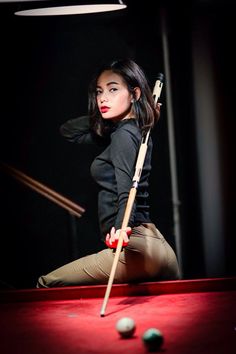 a woman leaning on a pool table with a cue in her hand and two balls behind her