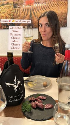 a woman sitting at a table holding a wine glass in front of her and some food on the plate