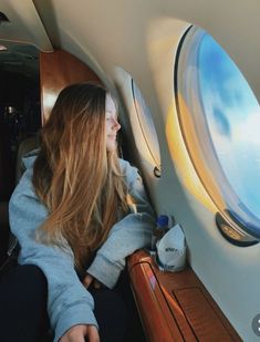 a woman sitting on an airplane looking out the window at the blue sky and clouds