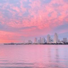 the city skyline is seen from across the water at sunset with pink clouds in the sky