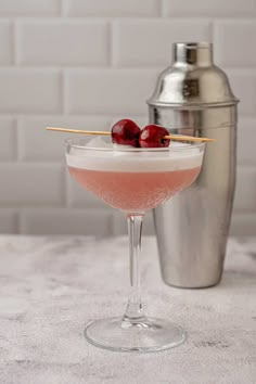 a martini with cherries in it on a table next to a cocktail shaker