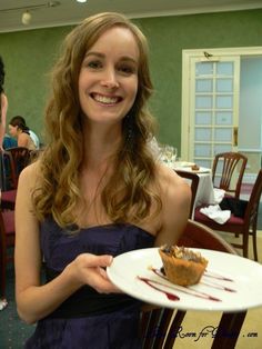 a woman in a purple dress holding a white plate with food on it and smiling at the camera