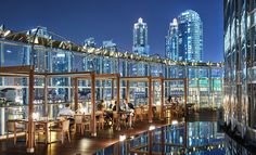 people are sitting at tables on the roof of a building with city lights in the background