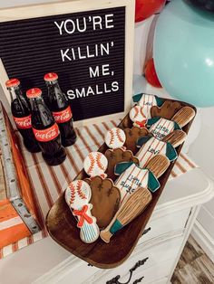 baseball themed cookies are on a table with balloons and signs in the background that say you're killin'me, smalls