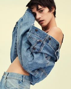 a woman with short black hair wearing a jean jacket and denim shorts, posing in front of a white background