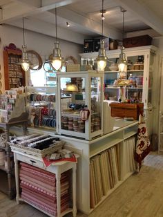 the inside of a quilt shop with lots of items on display and lights hanging from the ceiling