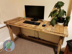 a wooden desk with a computer monitor and keyboard sitting on top of it next to a potted plant