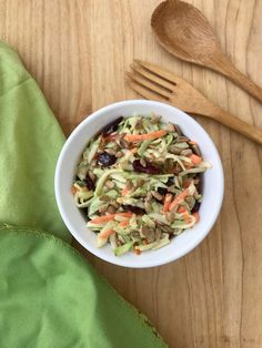 a white bowl filled with coleslaw and carrots next to a wooden spoon