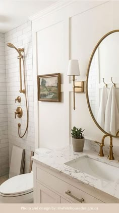 a white bathroom with gold fixtures and marble counter tops, along with a round mirror on the wall