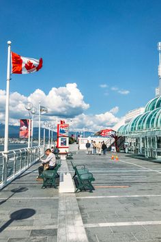 people are sitting on benches at the edge of a walkway near some buildings and flags