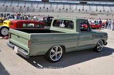 an old pick up truck parked next to other cars in a parking lot at a race track