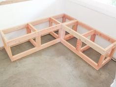 a corner bench made out of wood sitting on top of a cement floor next to a window