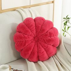 a pink flower shaped pillow sitting on top of a white couch next to a cup