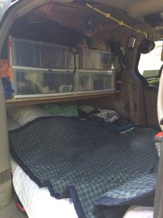 the bed in the back of a van is covered with blankets and other items for storage