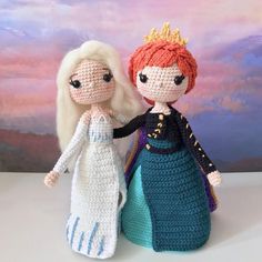 two crocheted dolls standing next to each other in front of a backdrop with clouds