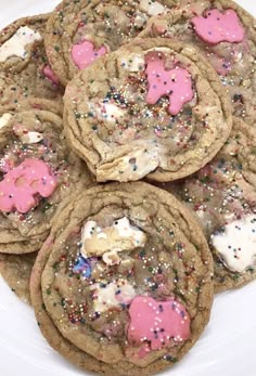 some cookies with pink and white frosting are on a plate next to sprinkles