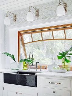 a kitchen with white cabinets and green plants in vases on the window sill