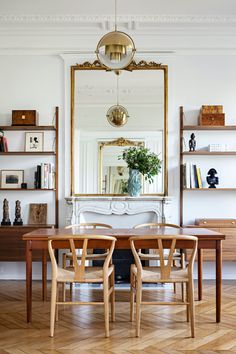 a dining room table with chairs and a large mirror above it, in front of a bookshelf