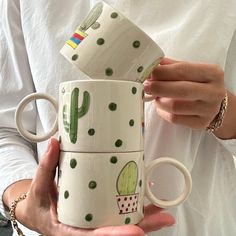 a woman holding three coffee mugs with cactus designs on them, one is white and the other has green polka dots