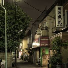 an alley way with buildings and trees on both sides, at night in the city