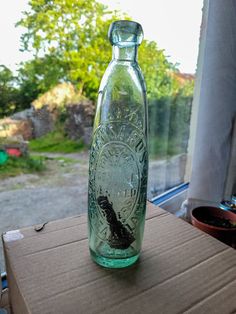 an empty glass bottle sitting on top of a cardboard box next to a window sill