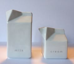 two white vases with the words milk and cream written on them sitting next to each other