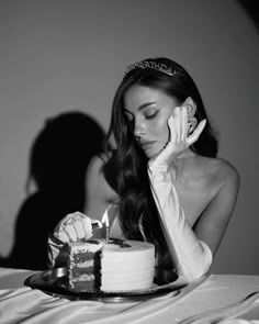 a woman sitting at a table with a cake in front of her and holding a cell phone to her ear