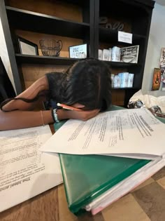 a young woman is sleeping on top of some books and papers in front of her