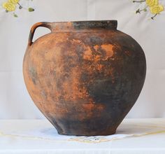 an old brown vase sitting on top of a table next to a yellow flower arrangement