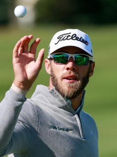 a man wearing sunglasses and a hat tossing a golf ball in the air with his hand