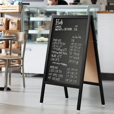 a blackboard sign in the middle of a room with tables and chairs behind it