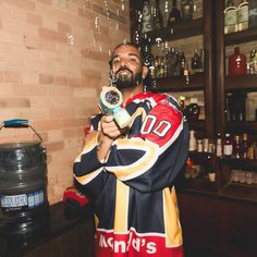 a man in a hockey jersey is holding a drink and looking at the camera while standing next to a brick wall