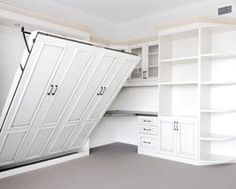 an empty room with white cupboards and shelves on the wall, under a slanted ceiling