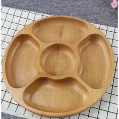 a wooden plate with six compartments on top of a place mat next to a pink flower