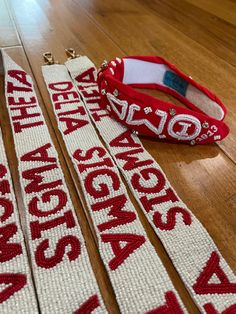 two red and white bracelets sitting on top of a wooden floor next to a pair of scissors