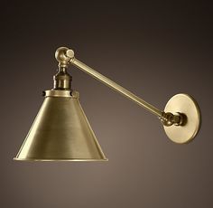 an antique brass swing arm wall light with a white shade on the side and a brown background