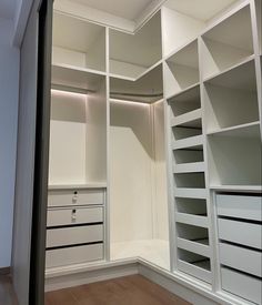 an empty walk in closet with white shelves and drawers