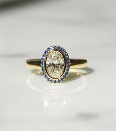 a yellow gold ring with blue and white stones on it's side, sitting on a table