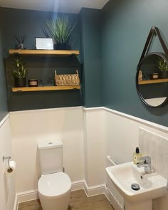 a white toilet sitting next to a sink in a bathroom under a mirror with shelves above it