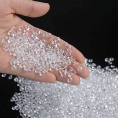 a hand holding some clear beads in front of a black background with water droplets on it