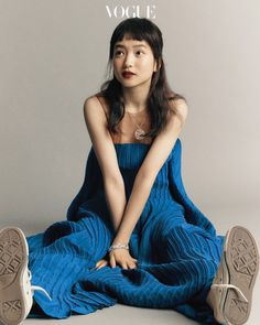 a woman sitting on the ground with her legs crossed in front of her, wearing a blue dress