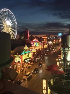 a city street filled with lots of traffic next to tall buildings and ferris wheel at night